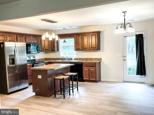a kitchen with stainless steel appliances granite countertop a refrigerator a stove a sink a dining table and chairs with wooden floor