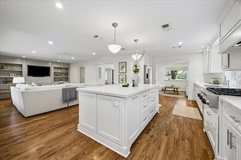 a large white kitchen with a large counter top a sink a stove and wooden floor