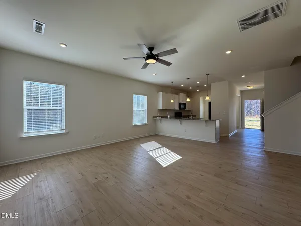 an empty room with wooden floor a kitchen view and windows