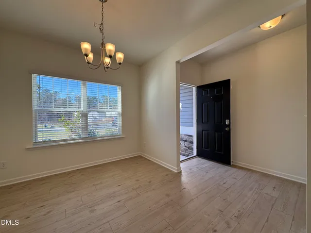 an empty room with wooden floor chandelier and windows