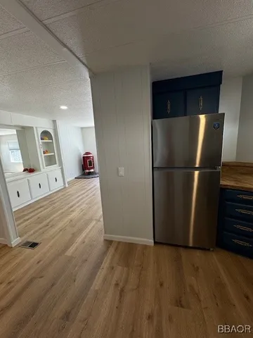 a view of a refrigerator in kitchen and an empty room with wooden floor
