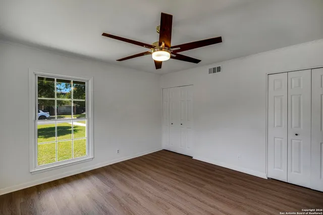 an empty room with wooden floor chandelier fan and windows