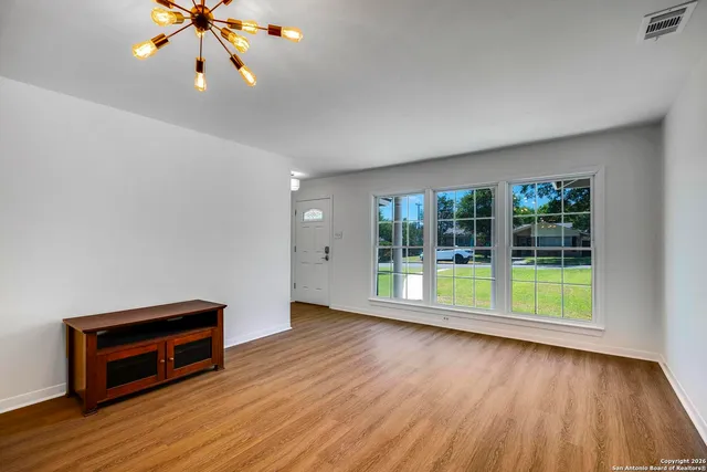 a view of an empty room with wooden floor and a window