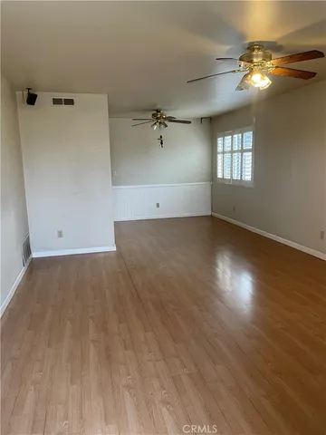 an empty room with wooden floor chandelier fan and windows