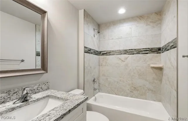 a bathroom with a granite countertop bathtub shower sink vanity and toilet