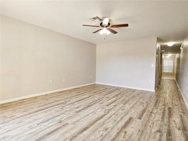 a view of empty room with wooden floor and fan