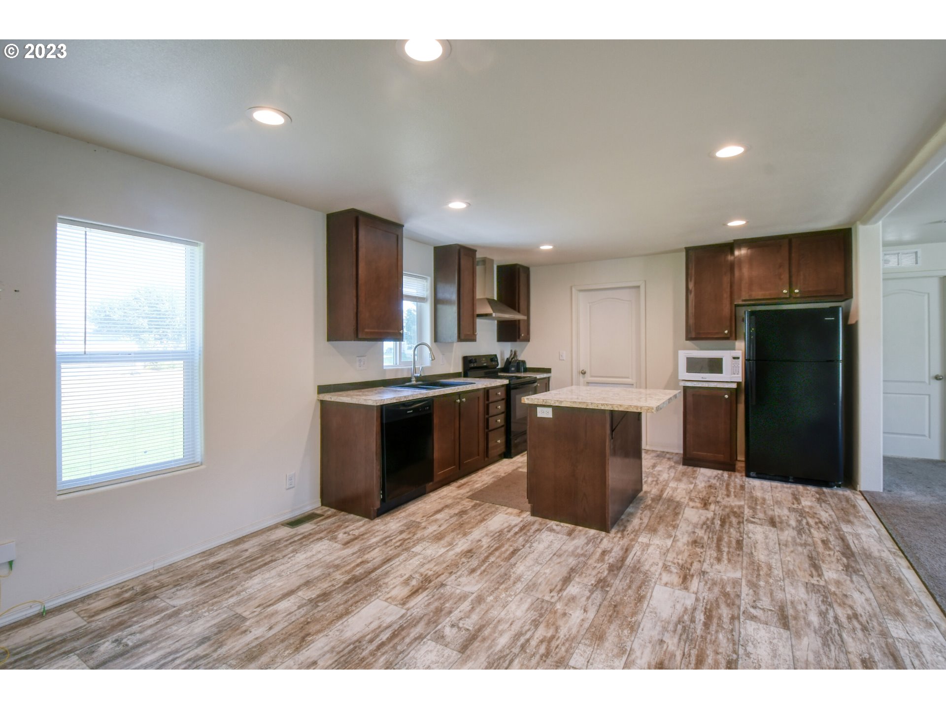 301 Northwest 3rd Street Boardman, OR 97818 - Photo 8 of 31 a kitchen with stainless steel appliances kitchen island granite countertop a refrigerator a sink and a stove top oven with wooden floor
