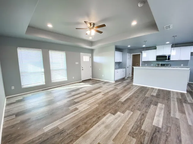 a view of an empty room and kitchen with wooden floor
