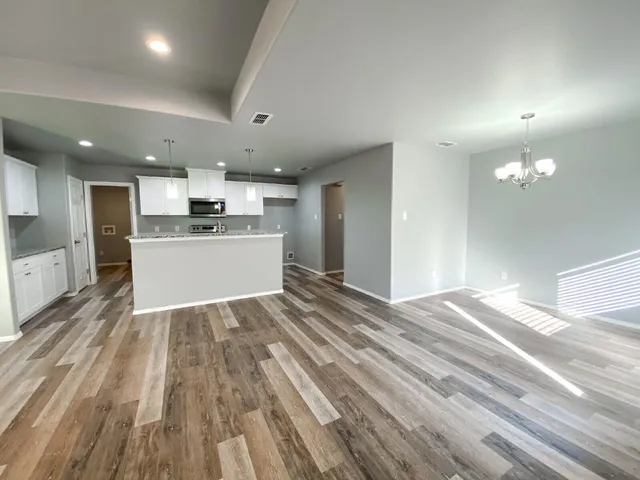 a large kitchen with kitchen island a stove a sink dishwasher a refrigerator and white cabinets with wooden floor