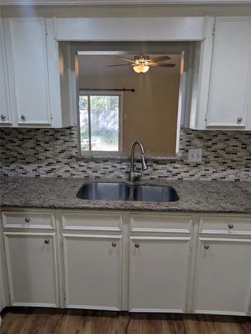 a sink with white cabinets granite counter tops and a wooden floor