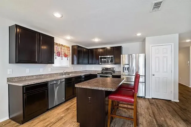 a kitchen with stainless steel appliances granite countertop a stove top oven a sink dishwasher a refrigerator and a dining table with wooden floor