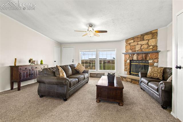 19290 Loop Road Colorado Springs, CO 80928 - Photo 6 of 39 Living room featuring ceiling fan, a fireplace, a textured ceiling, carpet flooring, and ornamental molding