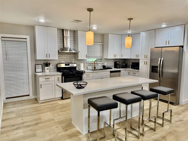 a kitchen with stainless steel appliances granite countertop a stove a refrigerator a sink a stove and white cabinets with wooden floor