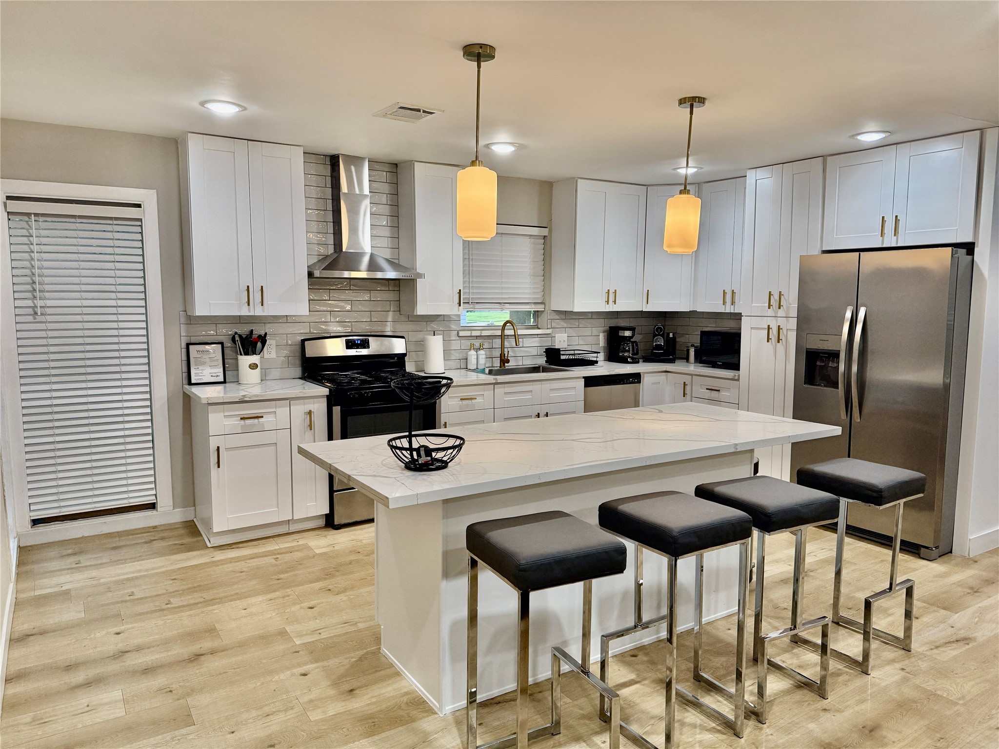 a kitchen with stainless steel appliances granite countertop a stove a refrigerator a sink a stove and white cabinets with wooden floor