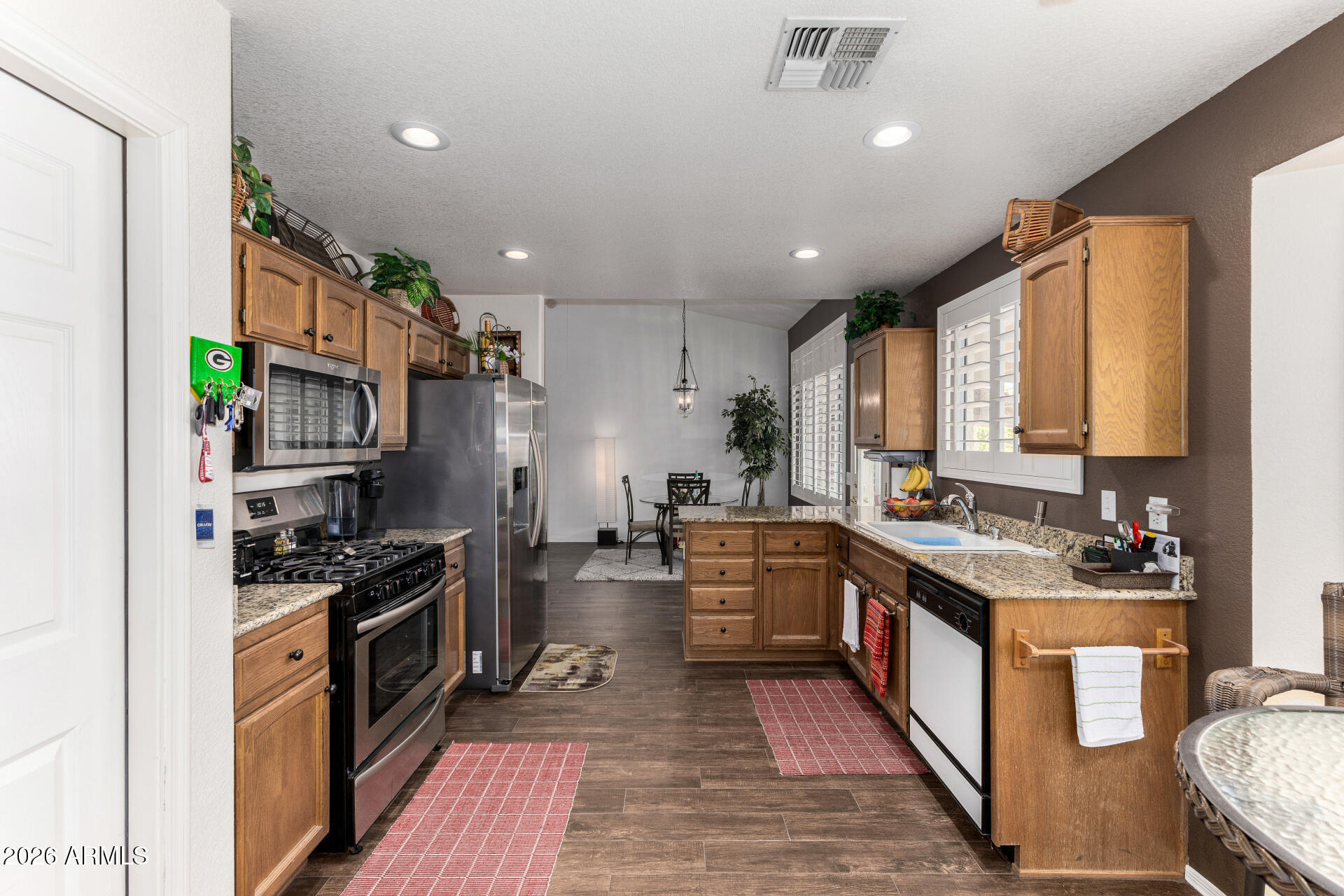 15764 Piccadilly Road Goodyear, AZ 85395 - Photo 10 of 31 a kitchen with stainless steel appliances granite countertop a stove top oven a sink dishwasher and a refrigerator with wooden floor