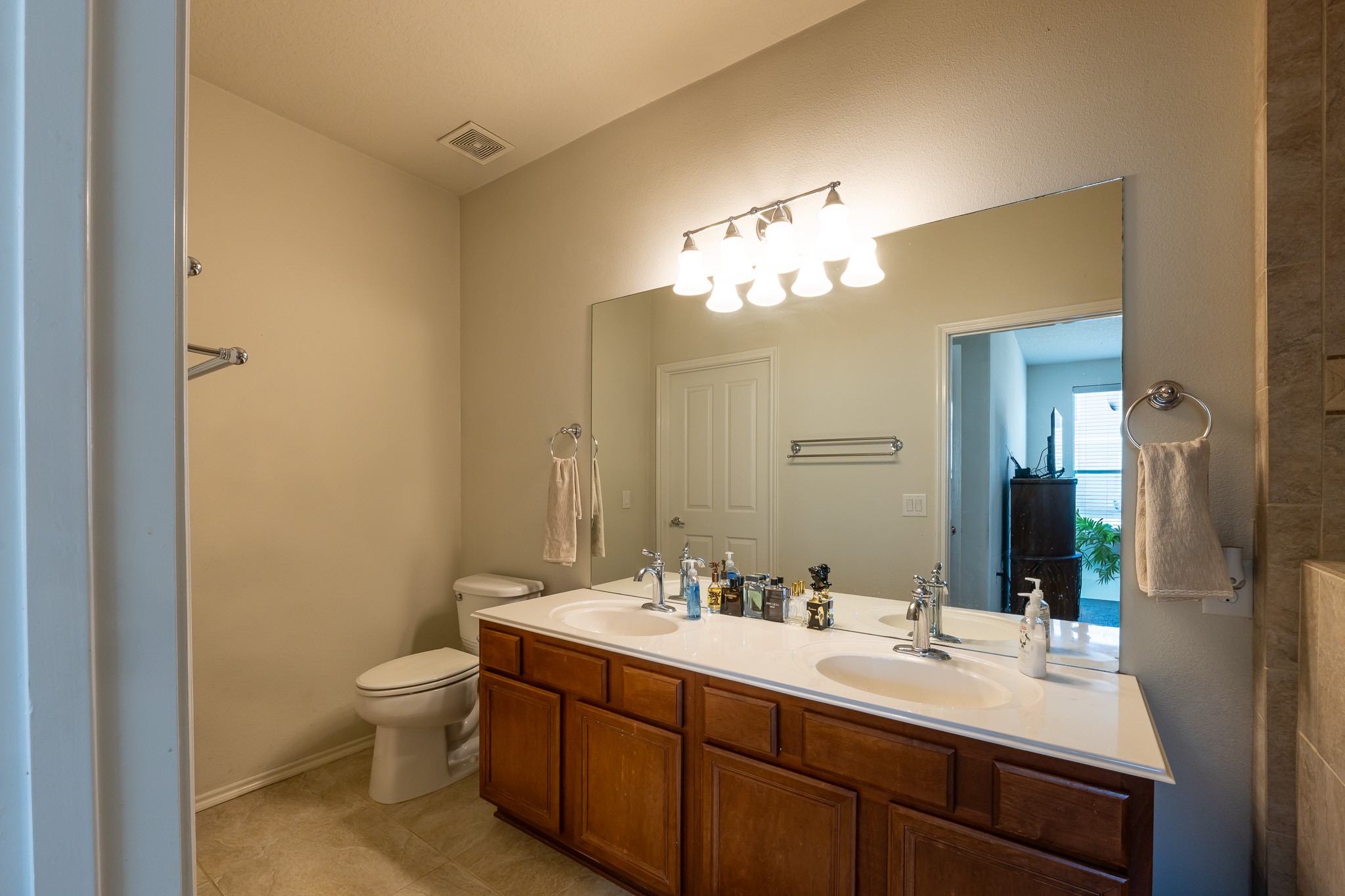 13600 Breton Ridge Street, Unit 29F Houston, TX 77070 - Photo 13 of 21 This bathroom features a large mirror, dual sinks with a spacious countertop, wooden cabinetry, and neutral tile flooring. It has modern lighting fixtures and access to a nearby room.
