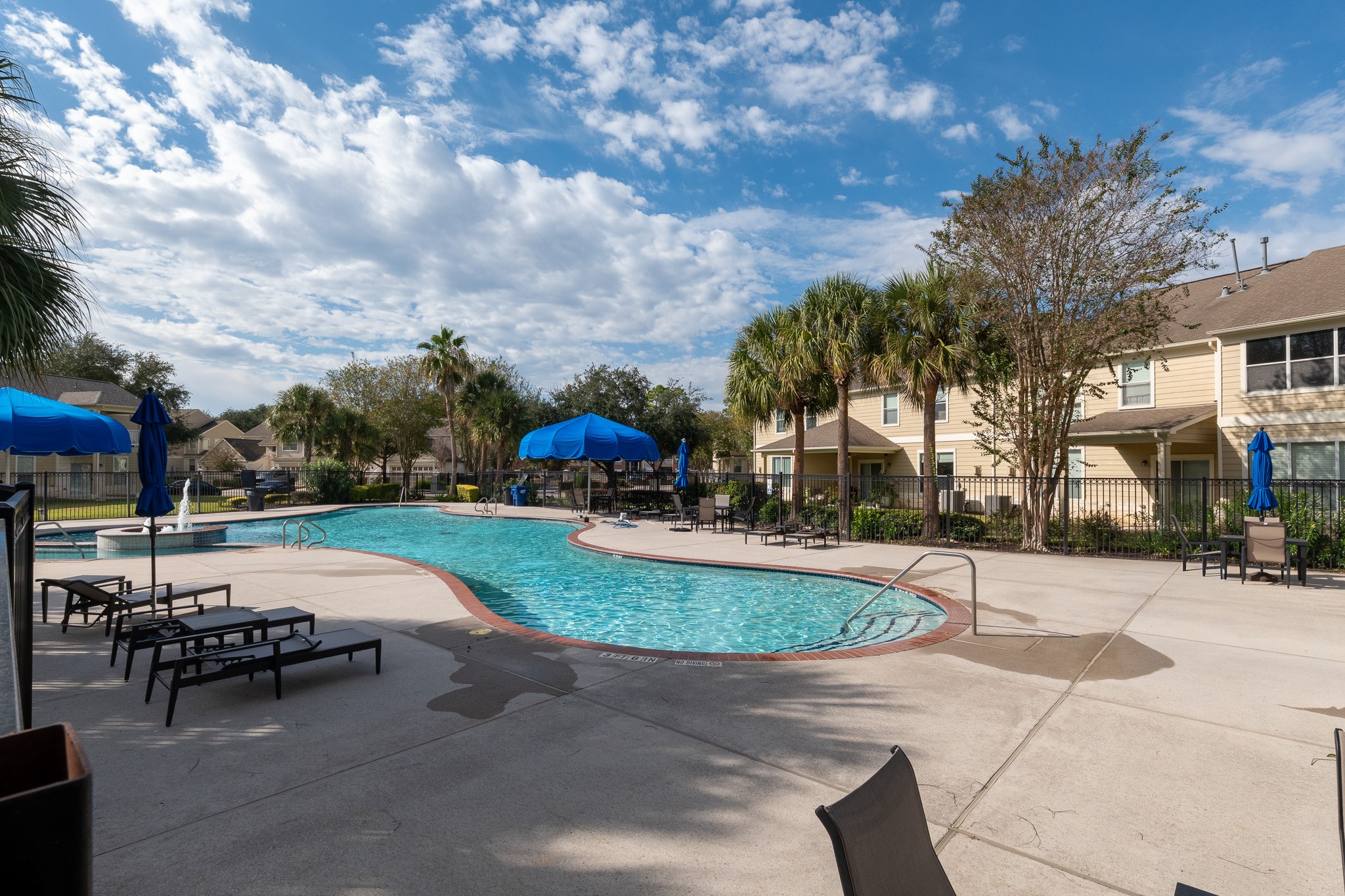 13600 Breton Ridge Street, Unit 29F Houston, TX 77070 - Photo 21 of 21 This photo showcases a well-maintained community pool area with lounge chairs, umbrellas, and surrounding greenery, set against a backdrop of condominiums. Perfect for relaxation and social gatherings.