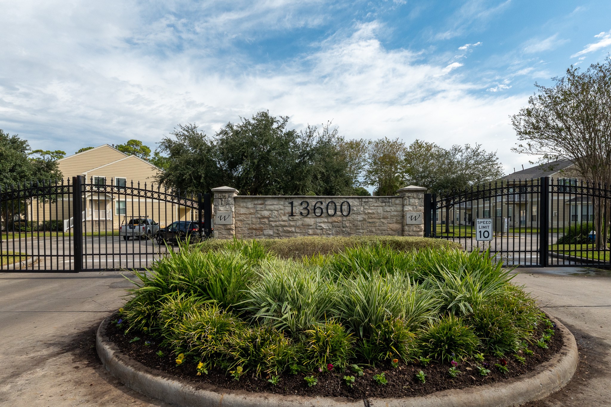 13600 Breton Ridge Street, Unit 29F Houston, TX 77070 - Photo 4 of 21 This photo shows a gated community entrance with a stone wall displaying the address "13600." The area is landscaped with greenery and the entrance has a speed limit sign, suggesting a secure and well-maintained environment.