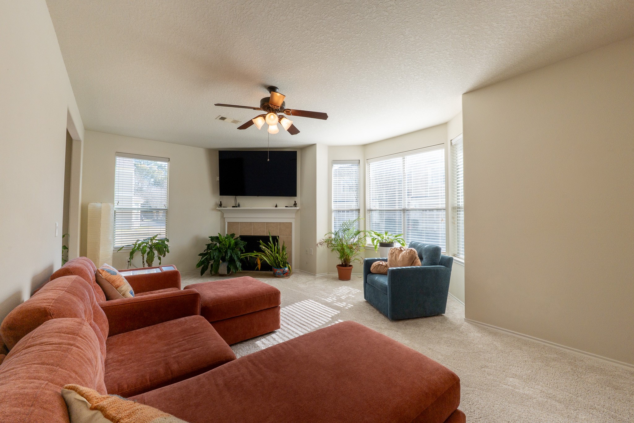 13600 Breton Ridge Street, Unit 29F Houston, TX 77070 - Photo 5 of 21 This cozy living room features a large living area, a fireplace with a mounted TV, and ample natural light from multiple windows. There's a ceiling fan for comfort and several potted plants adding a touch of greenery.