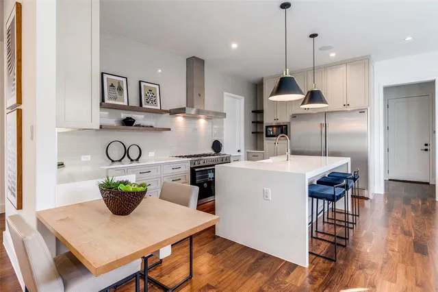 a kitchen with a refrigerator a stove a sink a dining table and chairs with wooden floor