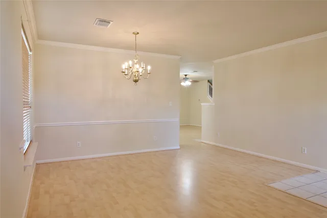 an empty room with chandelier fan and kitchen view