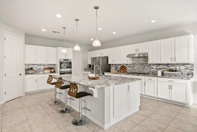 a kitchen with kitchen island granite countertop lots of white cabinets appliances and furniture