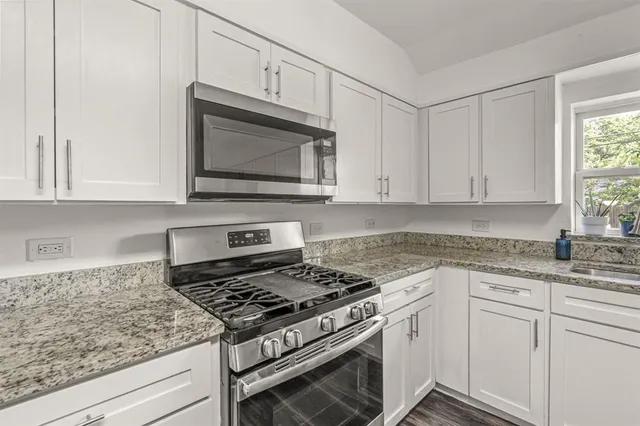 a kitchen with granite countertop white cabinets stainless steel appliances and a window