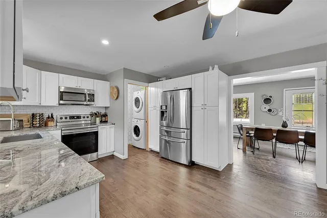 a kitchen with stainless steel appliances kitchen island granite countertop a refrigerator a stove a sink a dining table and chairs with wooden floor