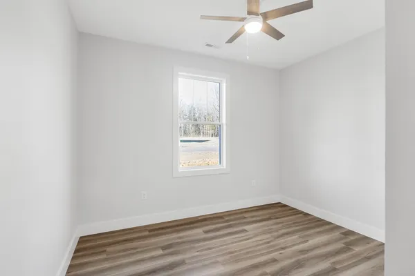 an empty room with wooden floor ceiling fan and windows