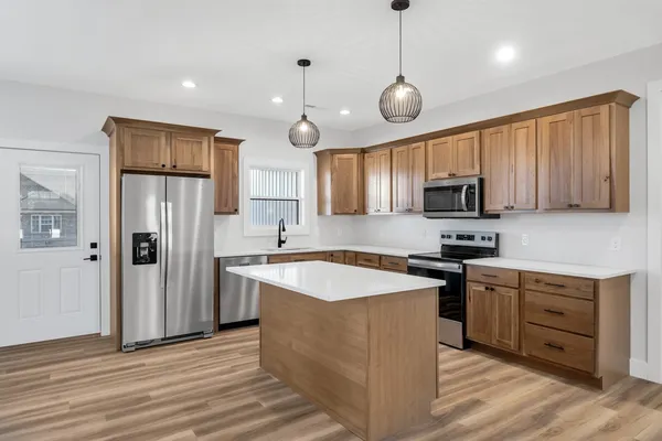 a kitchen with stainless steel appliances granite countertop wooden cabinets a refrigerator a sink a stove a microwave and wooden floors