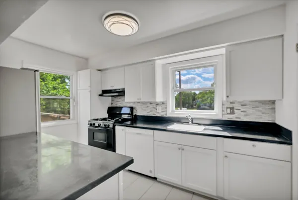a kitchen with granite countertop a stove a sink a window and cabinets