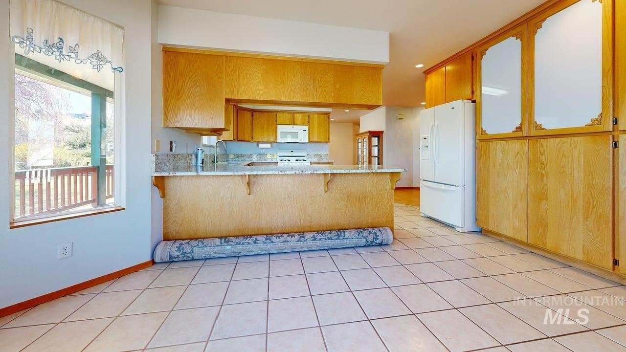 2794 9th Avenue Clarkston, WA 99403 - Photo 5 of 34 Kitchen featuring a peninsula, white appliances, a kitchen bar, wood finish cabinetry, and light tile patterned floors