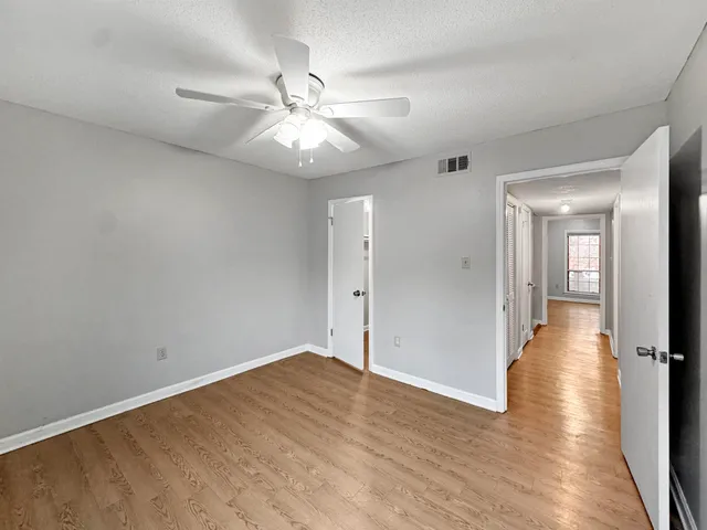an empty room with wooden floor fan and windows