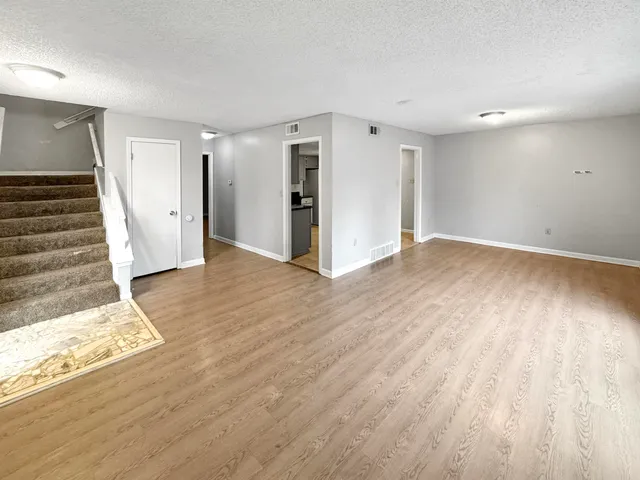 a view of an empty room with wooden floor and stairs
