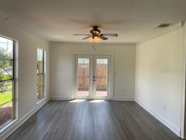 an empty room with wooden floor chandelier fan and windows