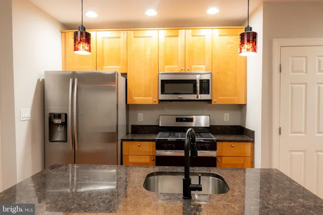 a kitchen with stainless steel appliances granite countertop a refrigerator a stove and a sink with wooden floor