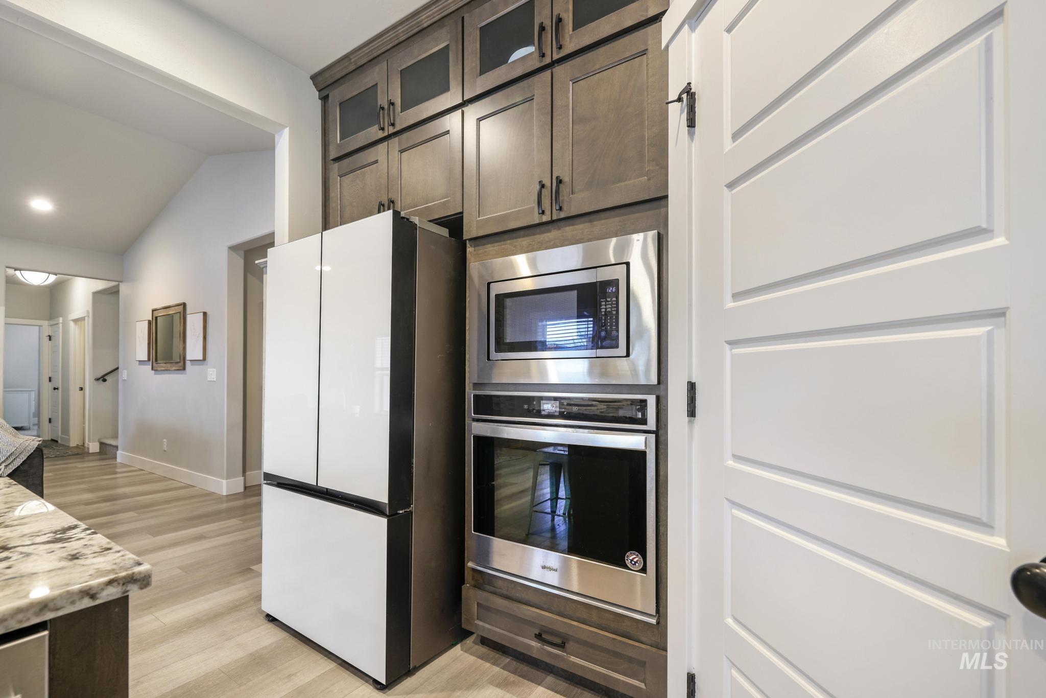 3103 Moonrise Road Twin Falls, ID 83301 - Photo 11 of 42 Kitchen featuring stainless steel appliances, vaulted ceiling, light wood-style flooring, dark wood finish cabinetry, and glass fronted cabinets