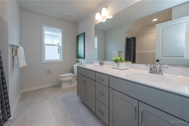 a spacious bathroom with double sink a toilet a window and shower