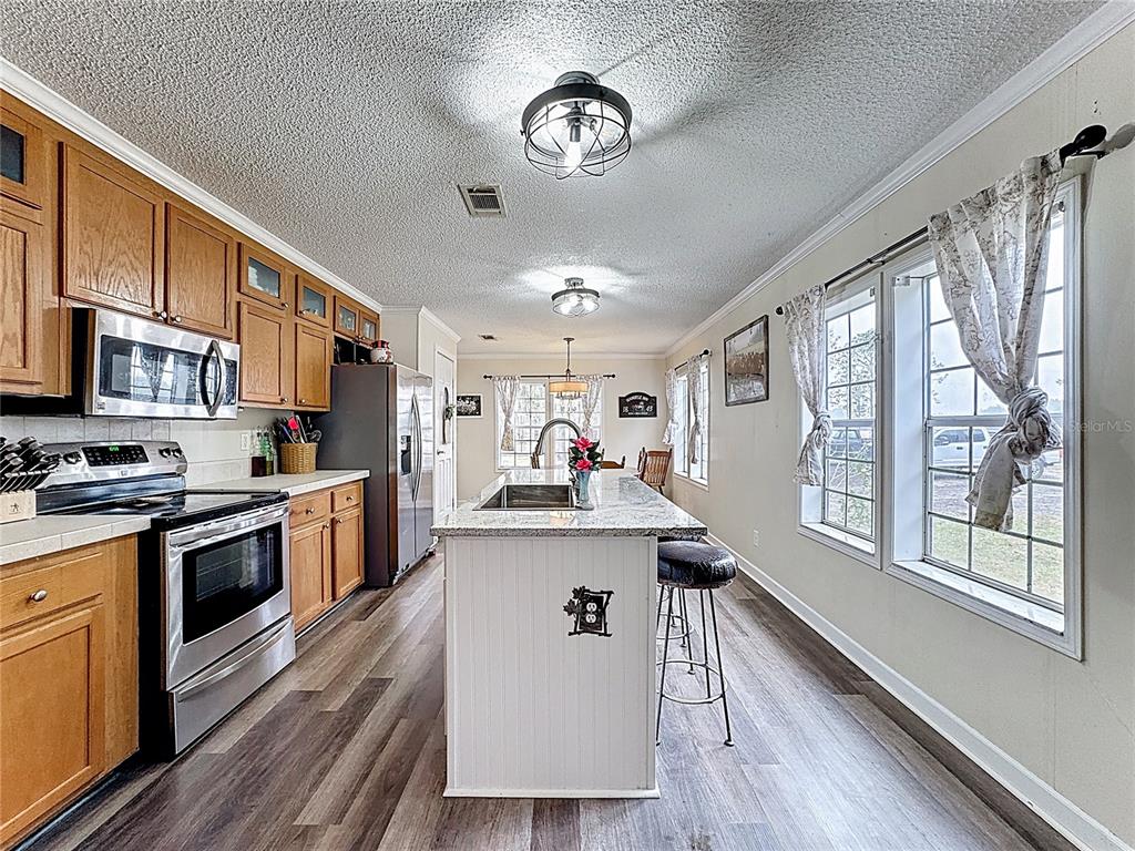 3230 Empire Church Road Groveland, FL 34736 - Photo 3 of 29 a open kitchen with stainless steel appliances granite countertop a stove top oven a refrigerator a dining table and chairs with wooden floor