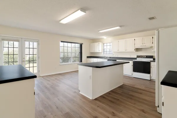 a kitchen with stainless steel appliances granite countertop white cabinets a sink a window and wooden floors