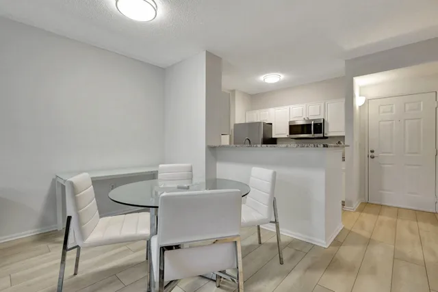 a kitchen with kitchen island granite countertop a dining table chairs refrigerator and cabinets