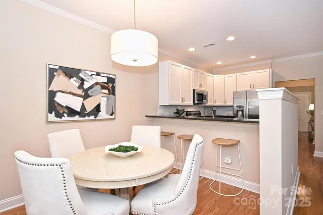 a kitchen with stainless steel appliances granite countertop a white refrigerator a microwave oven a dining table and chairs with wooden floor