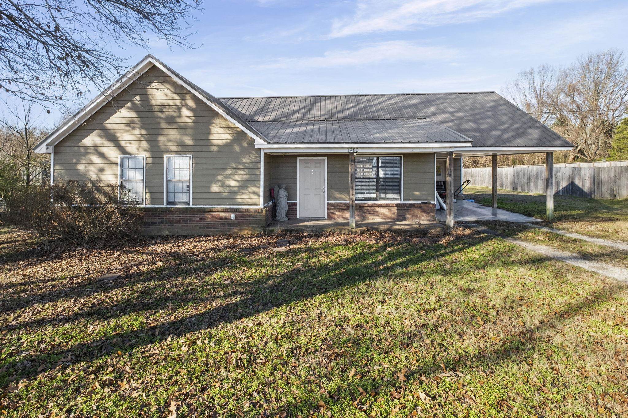 View of front of home featuring an attached carport, brick siding, a metal roof, and a porch