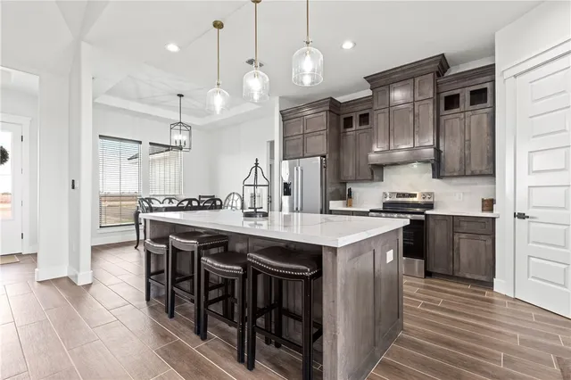 a kitchen with stainless steel appliances granite countertop a kitchen island a stove a refrigerator a sink a dining table and chairs with wooden floor