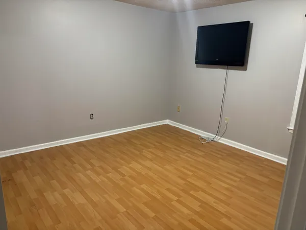 a view of an empty room with wooden floor and a flat screen tv