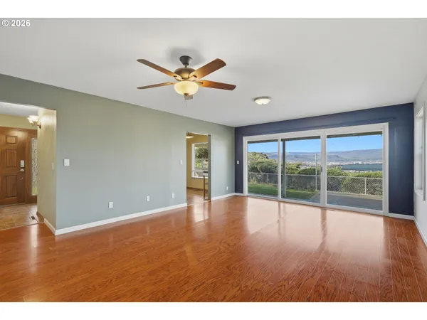 a view of an empty room with wooden floor and fan