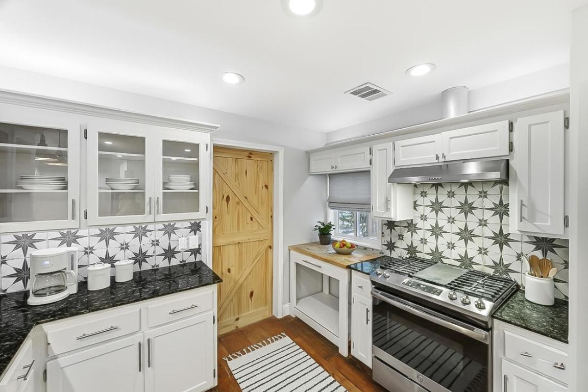 7804 Phoenix Pass Austin, TX 78737 - Photo 6 of 34 Kitchen with stainless steel gas range oven, white cabinets, dark wood-type flooring, decorative backsplash, and under cabinet range hood