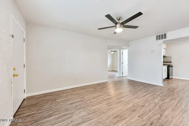a view of an empty room with wooden floor and a ceiling fan