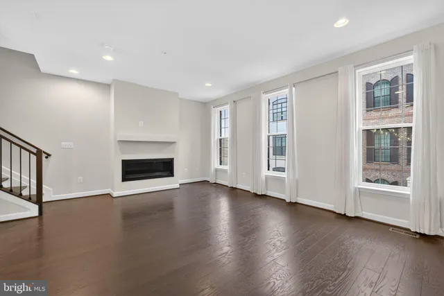 an empty room with wooden floor fireplace and windows
