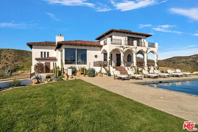 a living room with couches a fireplace and kitchen view with wooden floor